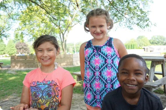 Three kids outdoors, smiling at the camera